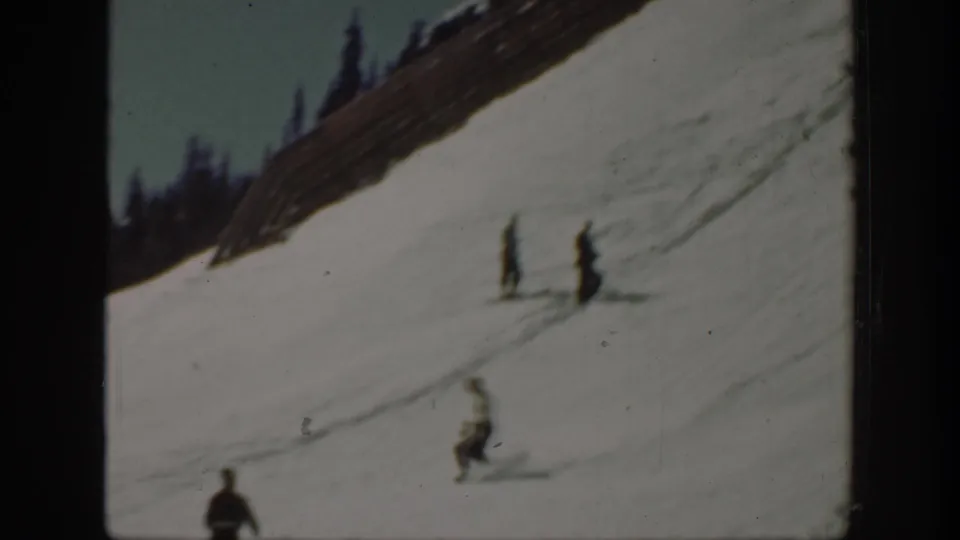 1940 Washington home-movie frame showing distant skiers on a snowy hillside with a fence and dark evergreens above.