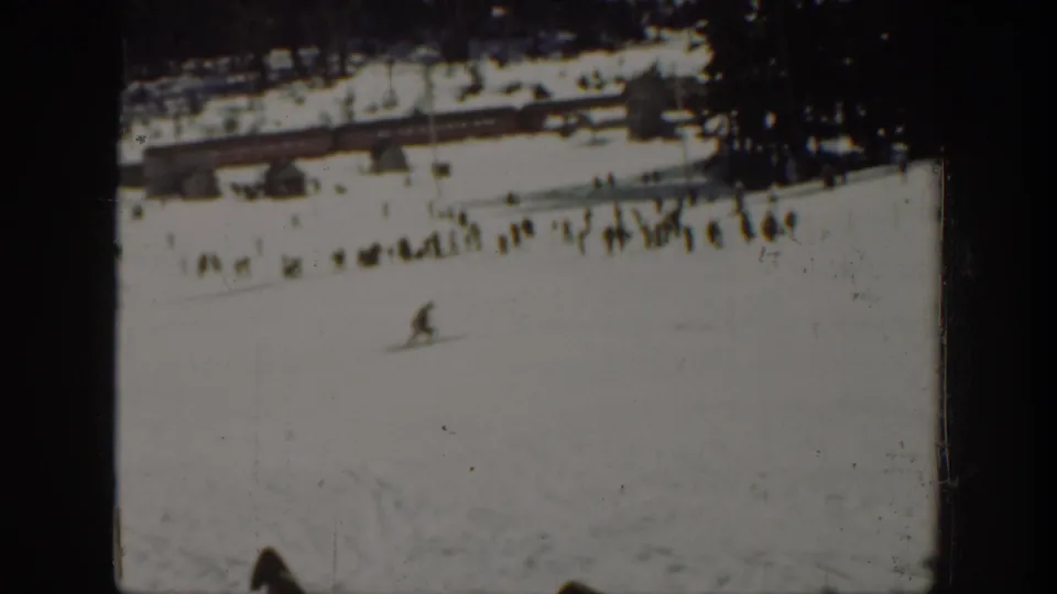 1940 Washington winter recreation frame with a skier on an open slope, distant onlookers, buildings, trees, and visible film wear.