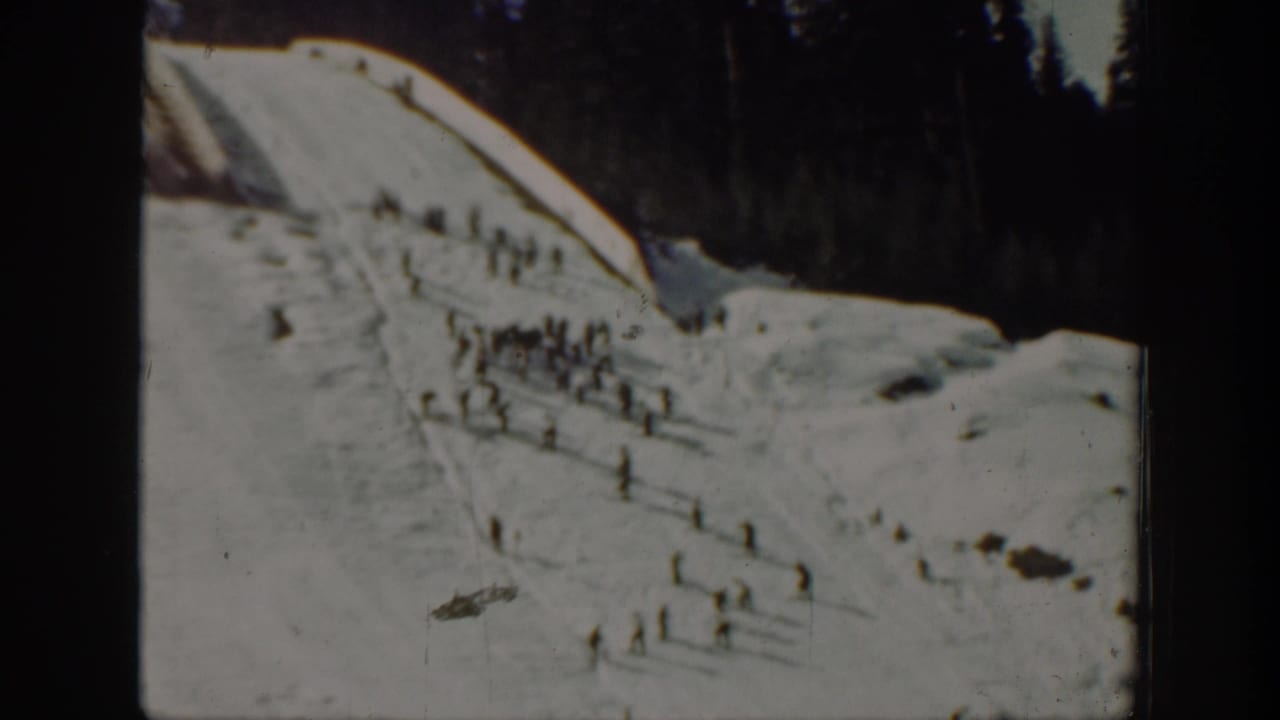 1940 Washington 8mm frame showing small distant figures skiing or standing on a snowy hillside with evergreens behind them.