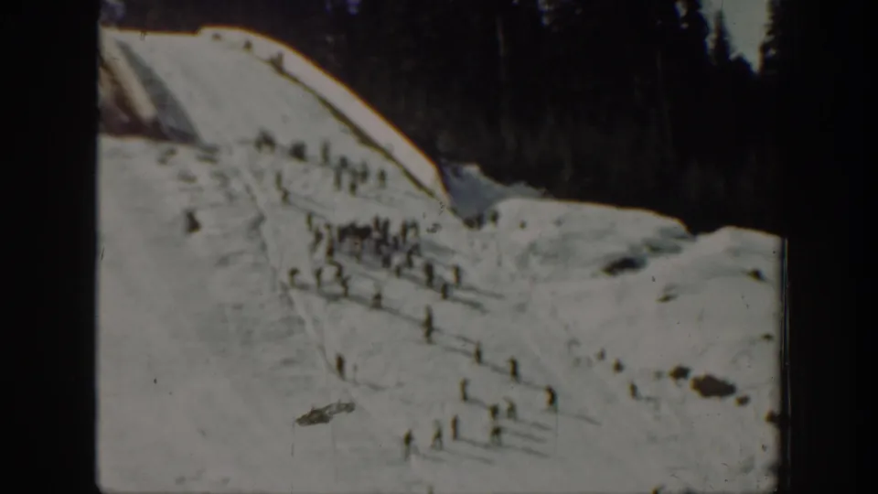 1940 Washington 8mm frame showing small distant figures skiing or standing on a snowy hillside with evergreens behind them.