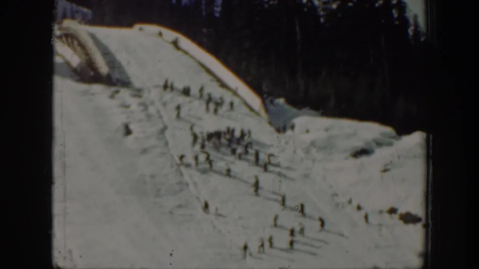 Distant 1940 Washington ski hill view with scattered people moving or standing on the snow below tall evergreens.