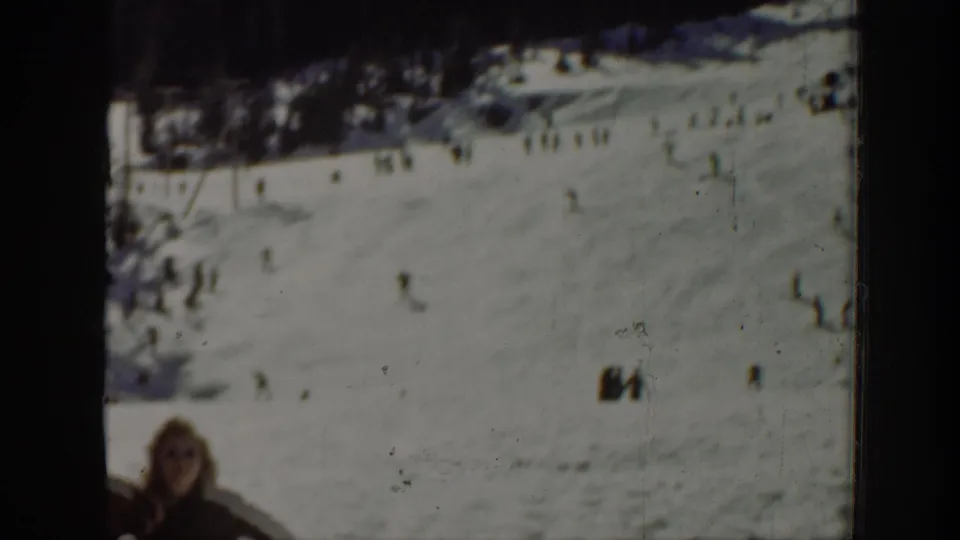 Wide 8mm home-movie frame from Washington in 1940 showing a snowy recreation slope with tiny skiers and a partial foreground person.