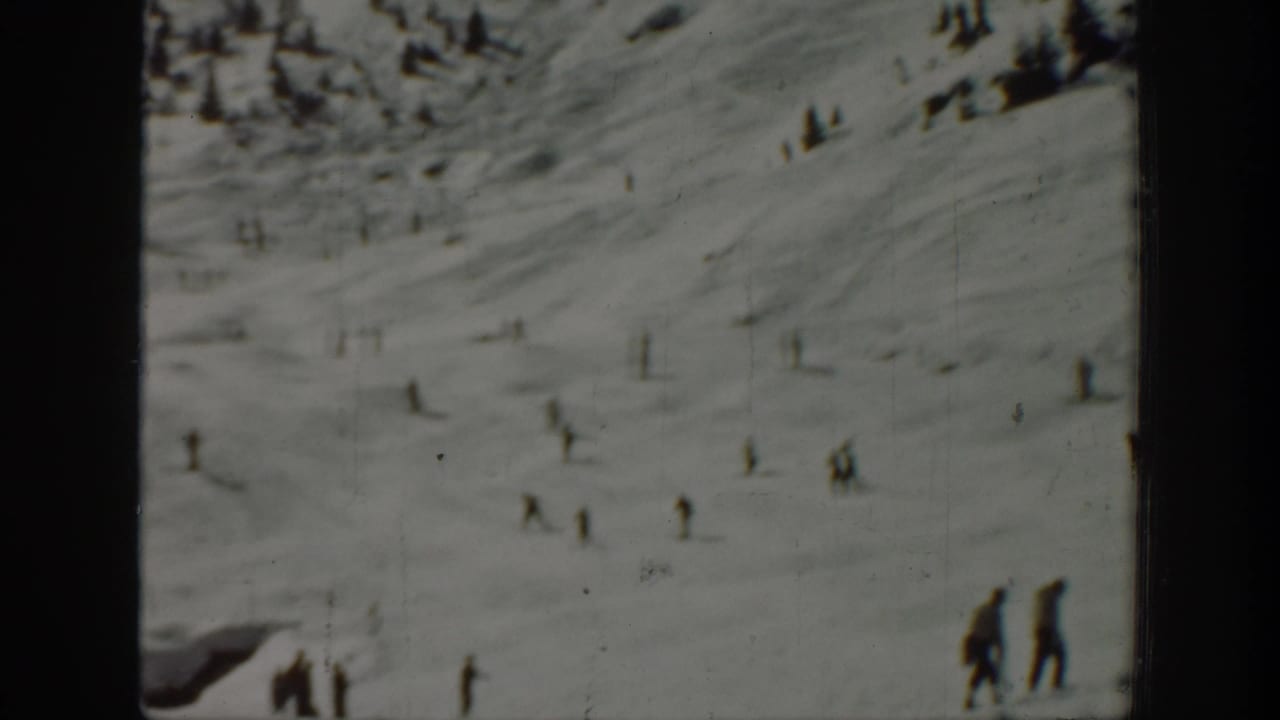 Wide 8mm view of a Washington ski slope, with small skiers spread across the snow and two closer figures near the right edge.