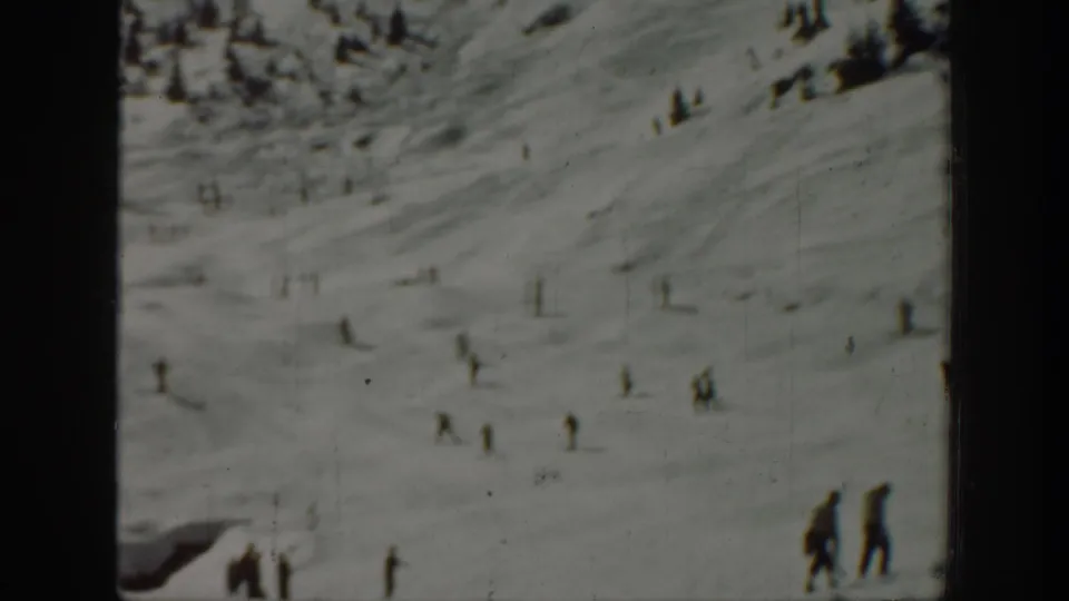 Wide 8mm view of a Washington ski slope, with small skiers spread across the snow and two closer figures near the right edge.