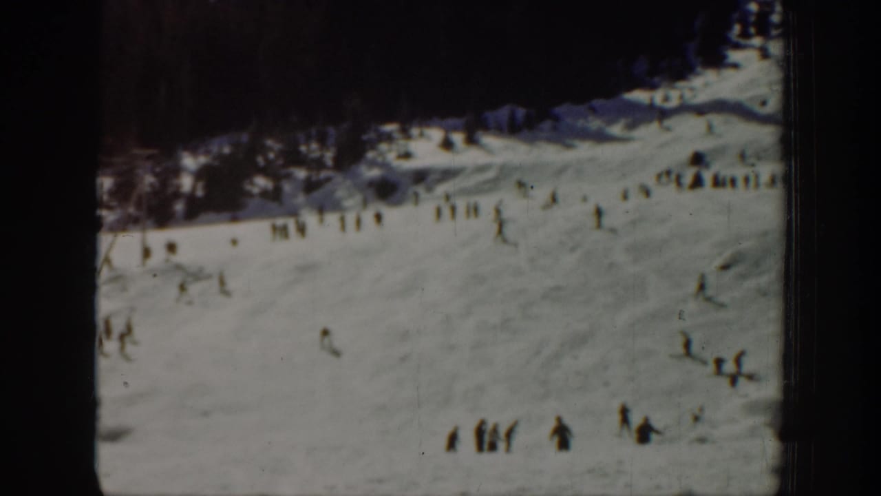 1940 Washington home-movie frame showing small figures on a snowy ski slope below a dark treeline.