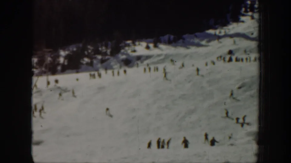 1940 Washington home-movie frame showing small figures on a snowy ski slope below a dark treeline.
