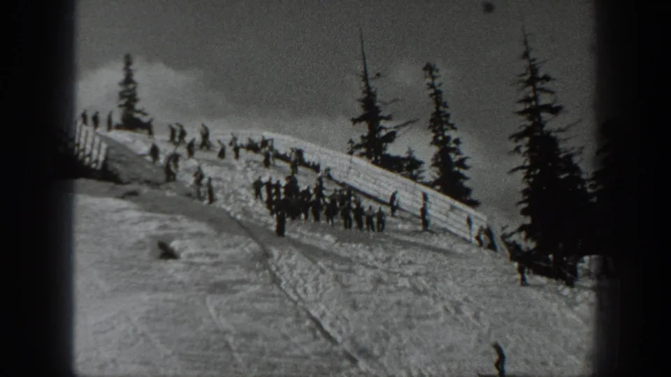 1940 Washington ski group near a wooden snow fence, with evergreen trees and tracked snow visible on the hillside.
