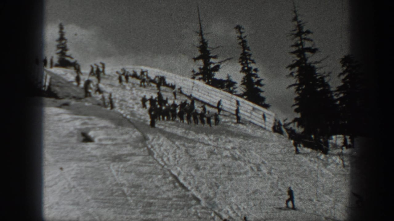 Black-and-white 1940 Washington home-movie frame showing people on a snowy ski slope near a fence and evergreens.
