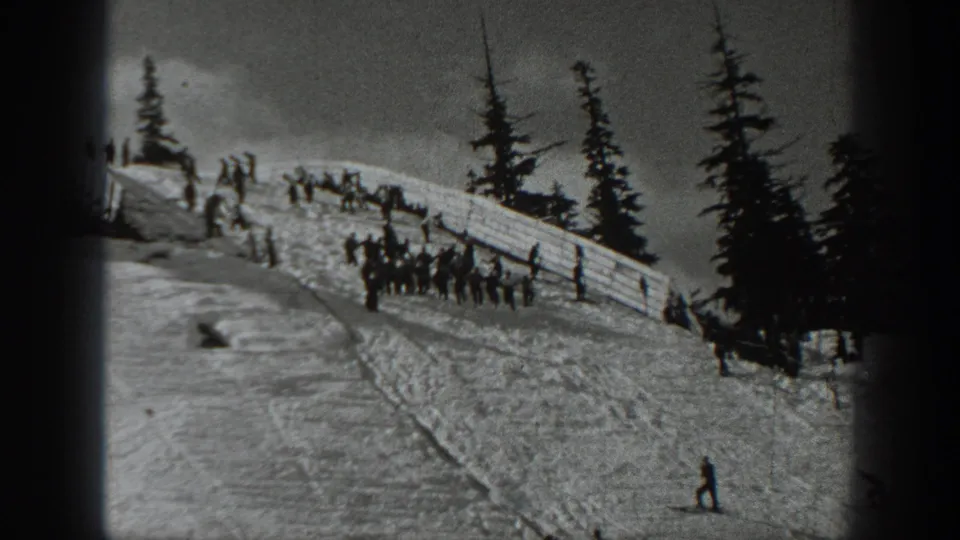 Black-and-white 1940 Washington home-movie frame showing people on a snowy ski slope near a fence and evergreens.