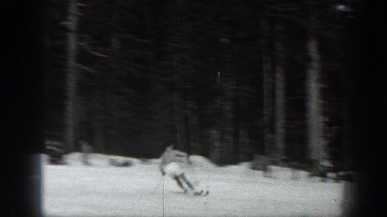Black-and-white 1940 Washington home-movie frame of a skier moving downhill on snow within a dense evergreen forest.