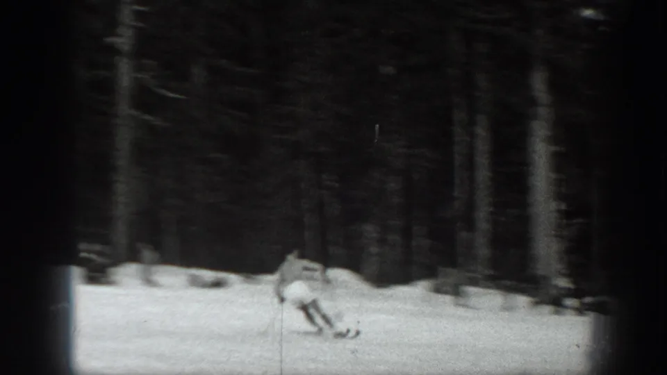 Black-and-white 1940 Washington home-movie frame of a skier moving downhill on snow within a dense evergreen forest.