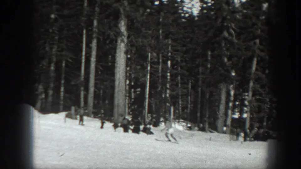 Black-and-white 1940 Washington frame showing small distant figures on a snow-covered forest slope with tall evergreens behind them.