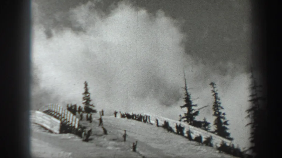Black-and-white 1940 Washington frame showing a snowy slope or overlook with distant people, evergreen trees, and rail-like fencing.