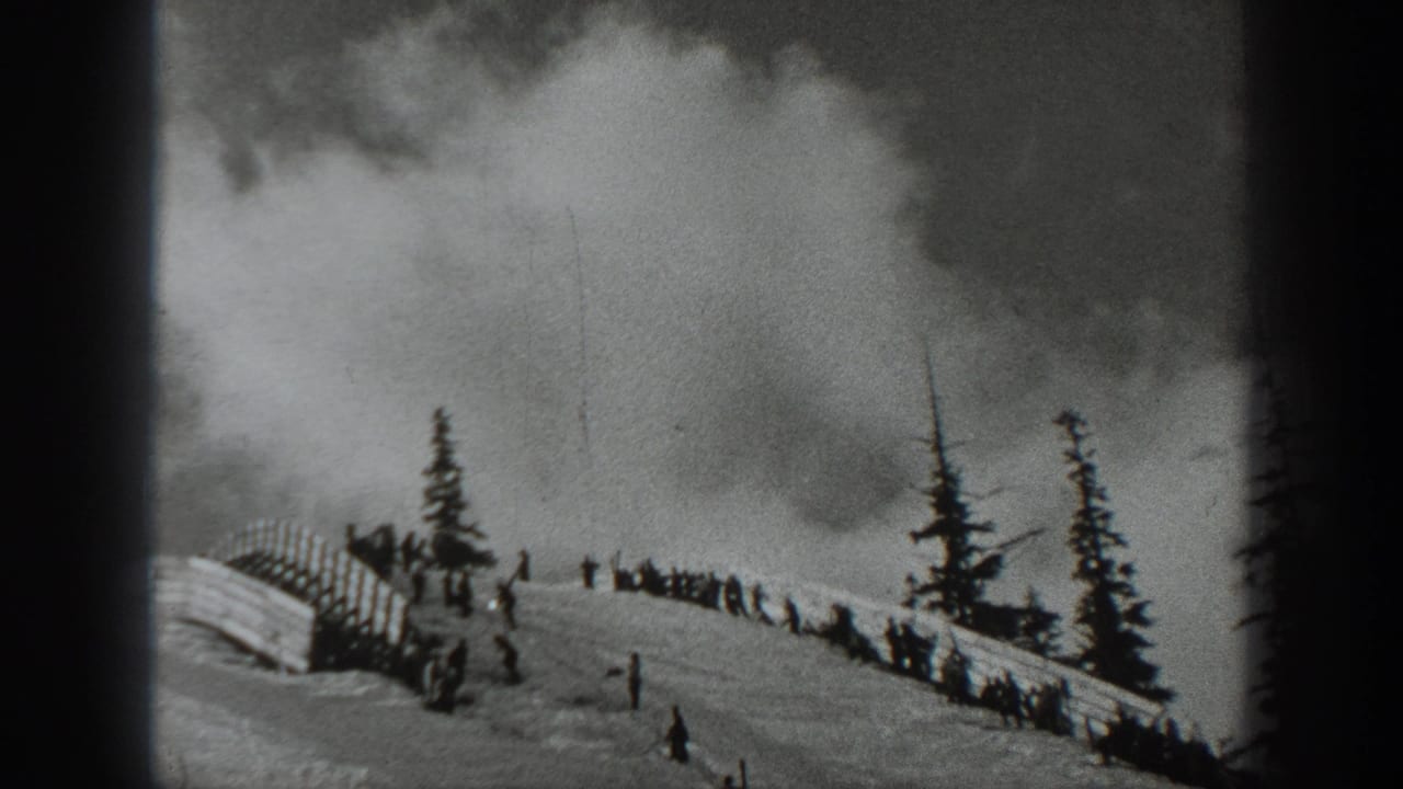 1940 Washington 8mm frame showing a snowy hillside, distant people, evergreen trees, fencing, and a rising smoke plume.