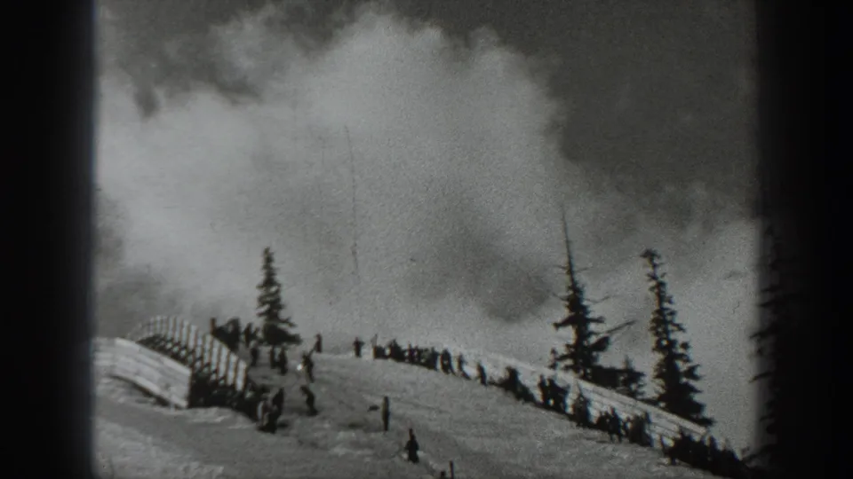 1940 Washington 8mm frame showing a snowy hillside, distant people, evergreen trees, fencing, and a rising smoke plume.