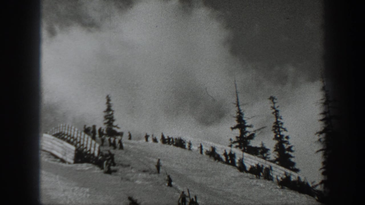 Snow-covered hillside with scattered people, trees, fencing, and thick smoke behind the ridge.
