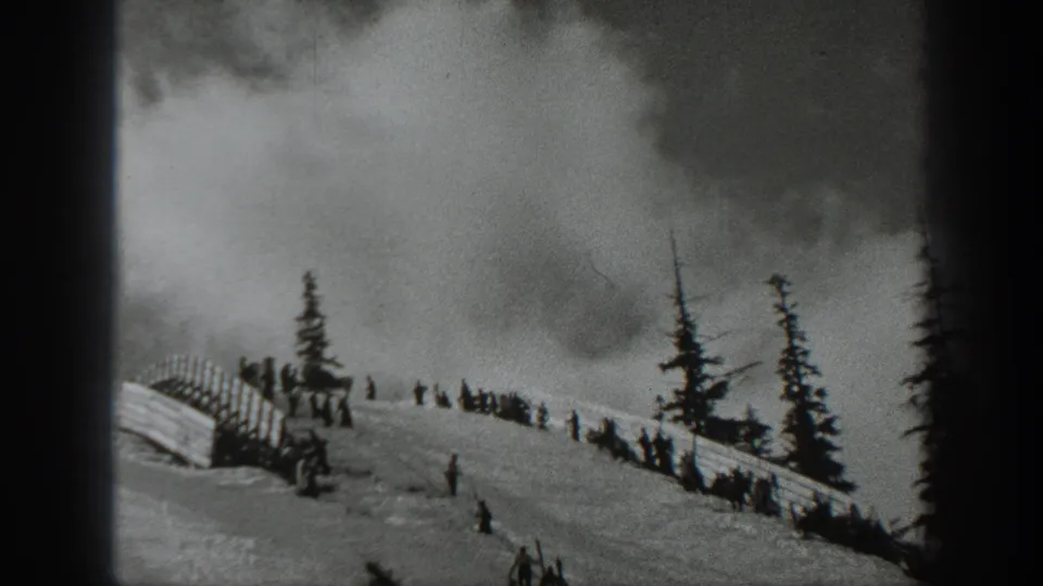 Washington home-movie frame from 1940 showing figures on a snowy slope as smoke spreads behind evergreens and fencing.