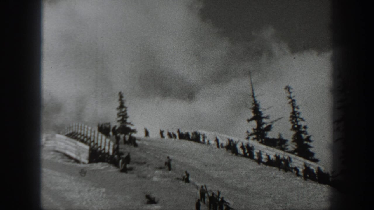 1940 Washington home-movie frame showing a snowy hillside, distant skiers, spectators by a wooden fence, evergreens, and a cloudy sky.