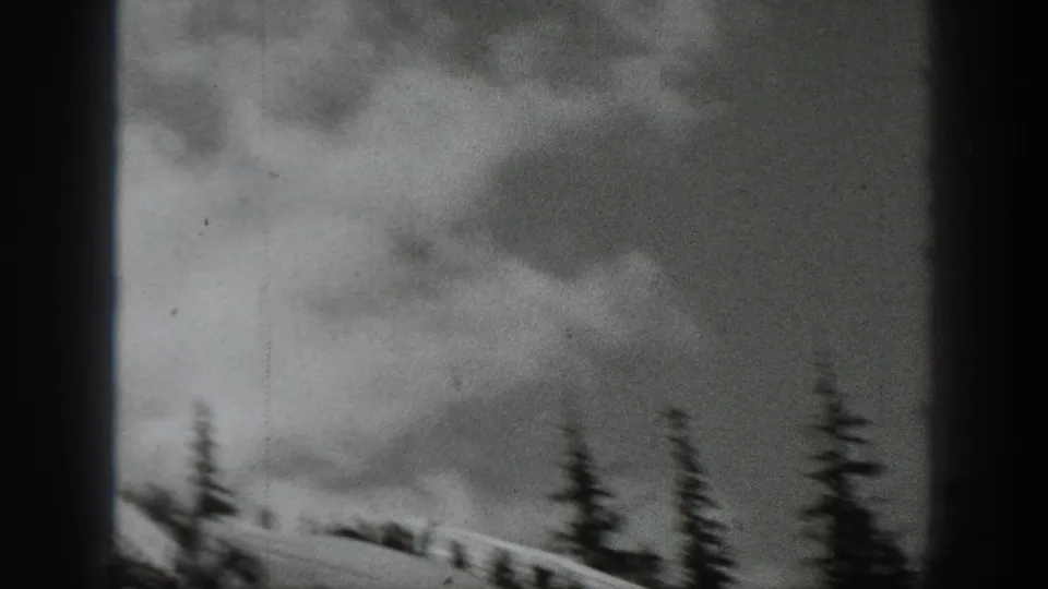 Soft, moving 8mm frame with a snowy mountain slope, evergreen silhouettes, cloudy sky, and partial dark frame edges.