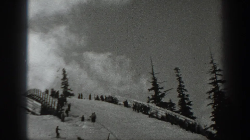 Black-and-white 1940 Washington home-movie view of skiers dispersed across a snow slope near fencing and tall evergreens.