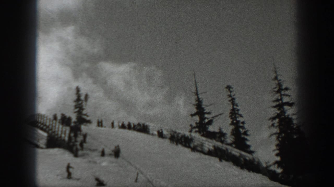 1940 Washington home-movie frame showing a snowy ski slope with evergreens, a wooden fence line, and distant people near the ridge.