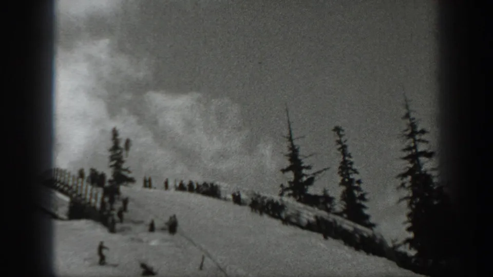 1940 Washington home-movie frame showing a snowy ski slope with evergreens, a wooden fence line, and distant people near the ridge.