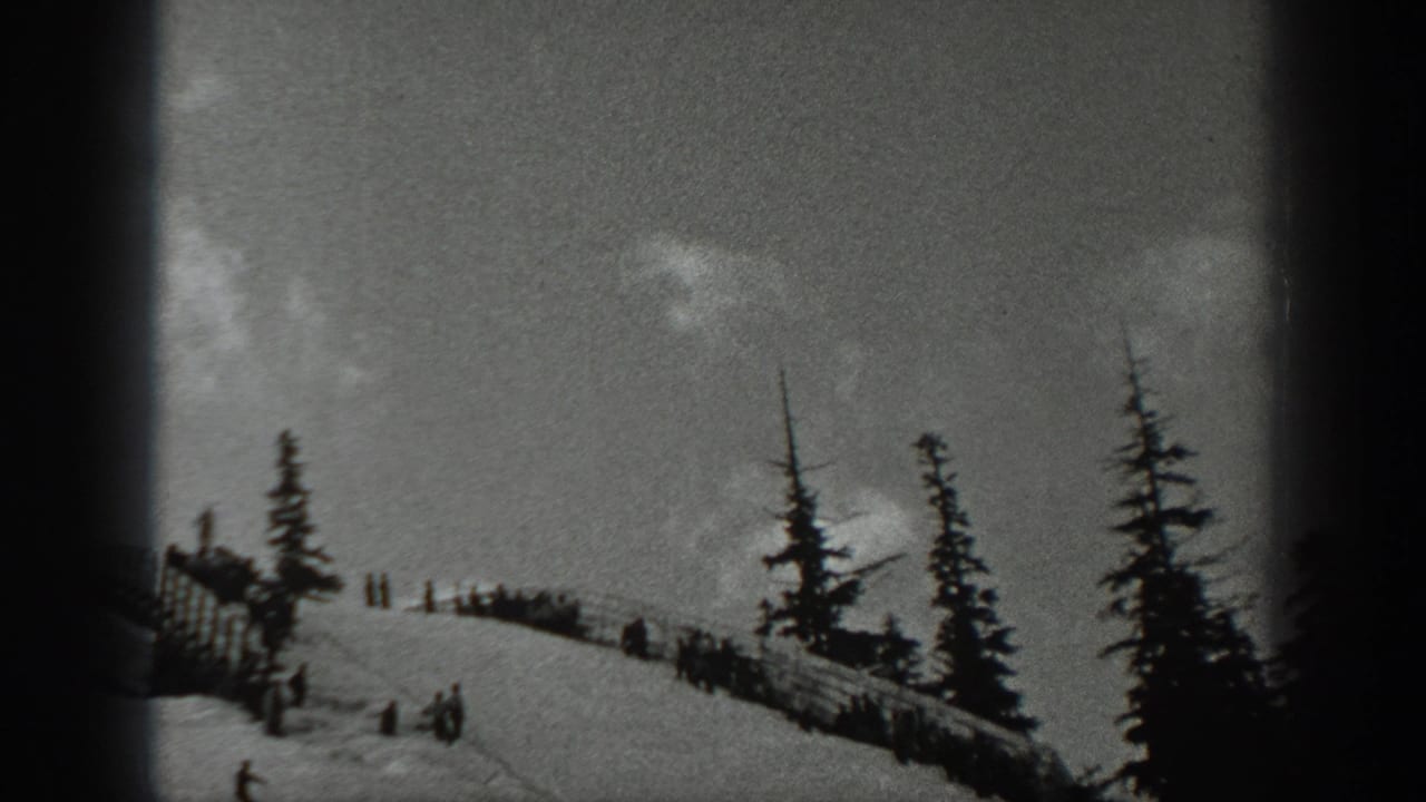 1940 Washington 8mm frame showing a snowy ski slope with evergreens, small figures on skis, and spectators near the crest.