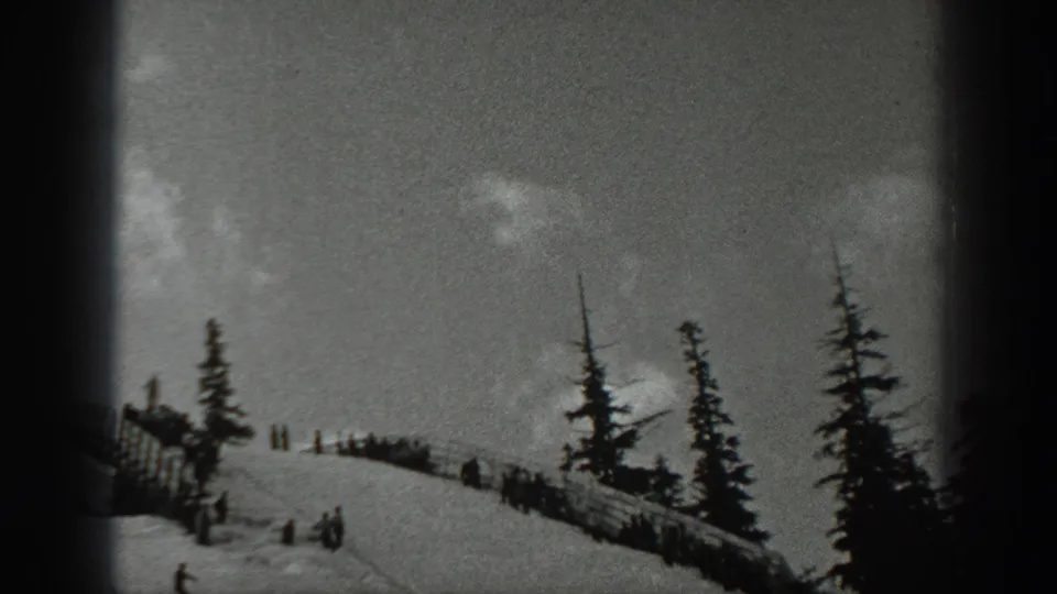 1940 Washington 8mm frame showing a snowy ski slope with evergreens, small figures on skis, and spectators near the crest.