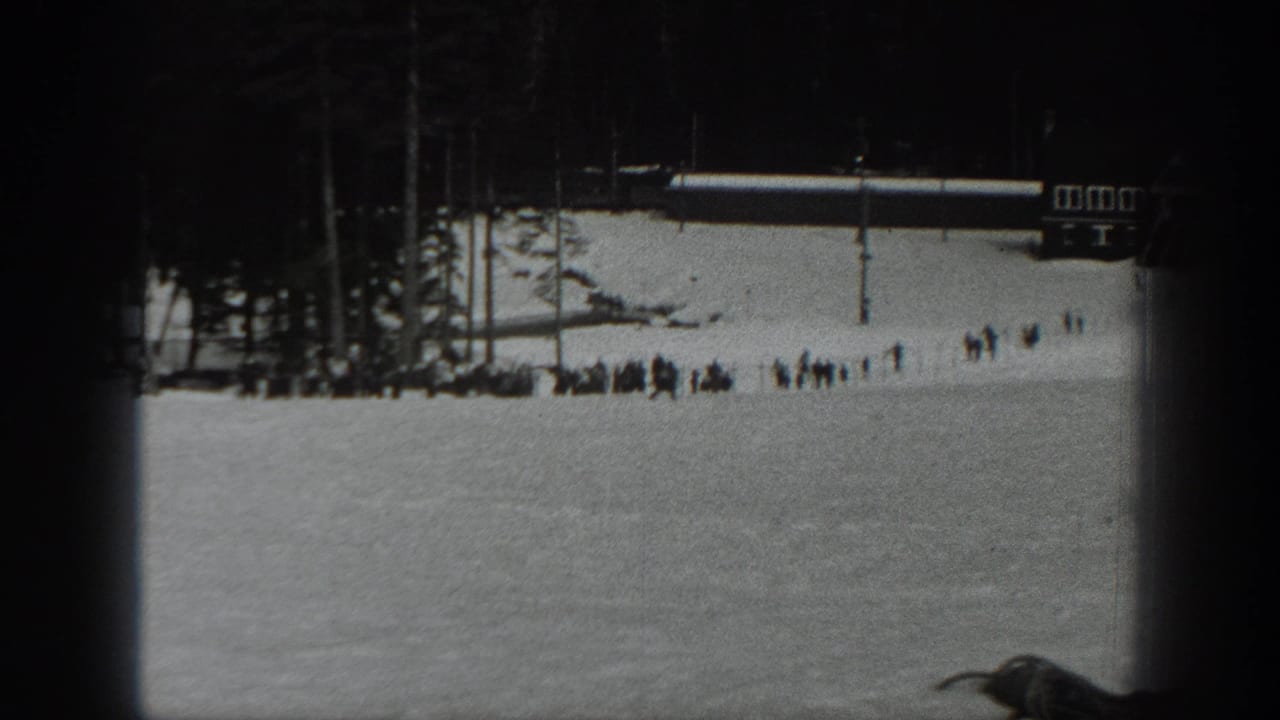 1940 Washington home-movie frame of a snowy ski slope with distant people gathered near trees and a small resort building.