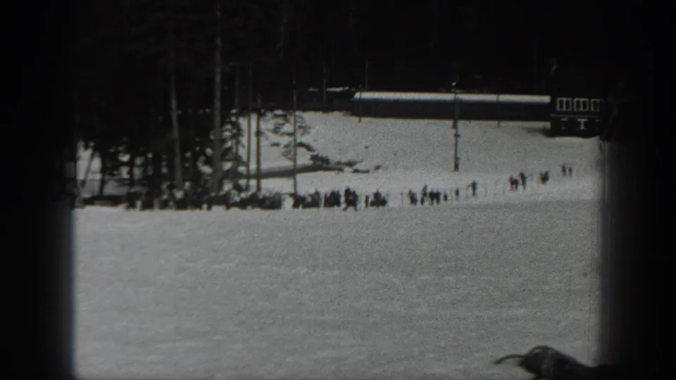 1940 Washington home-movie frame of a snowy ski slope with distant people gathered near trees and a small resort building.