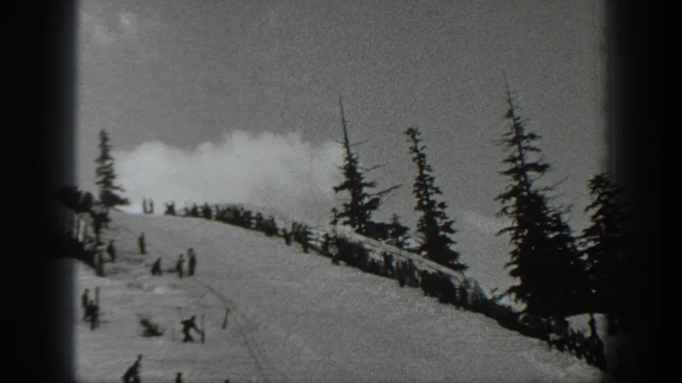 1940 Washington ski resort view with people spread along a snow ridge and dark evergreen trees on the mountainside.