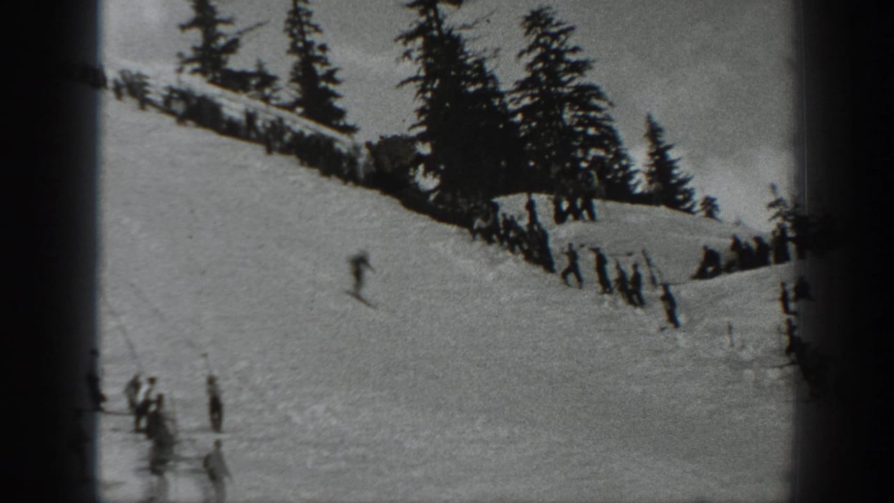 Black-and-white 1940 Washington home-movie frame of skiers on a snowy mountain slope below evergreens and a ridge fence.