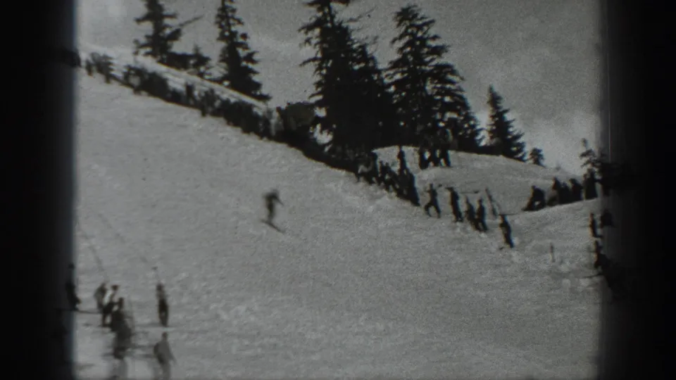 Black-and-white 1940 Washington home-movie frame of skiers on a snowy mountain slope below evergreens and a ridge fence.
