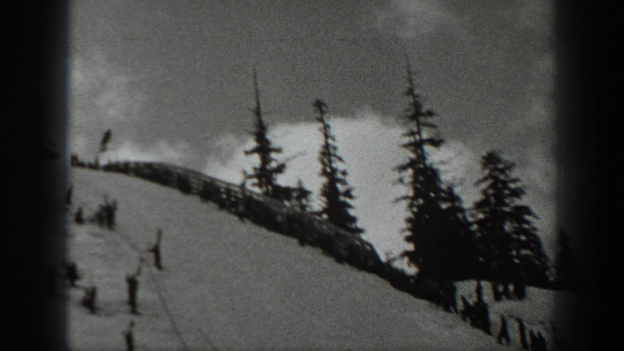 Snowy ridge with scattered skiers, evergreen trees, and a fence line.