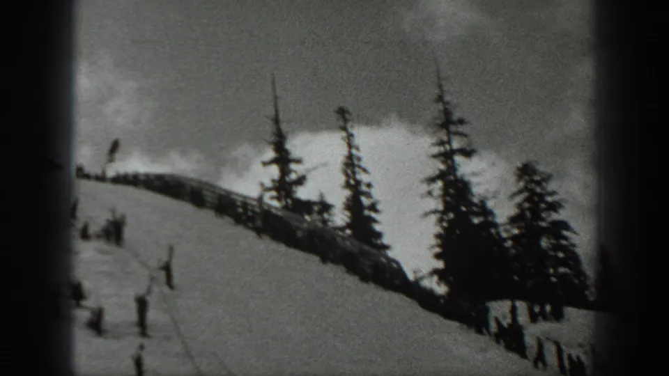 Black-and-white frame showing distant skiers on a Washington snow slope with evergreens and a dark vertical film edge.