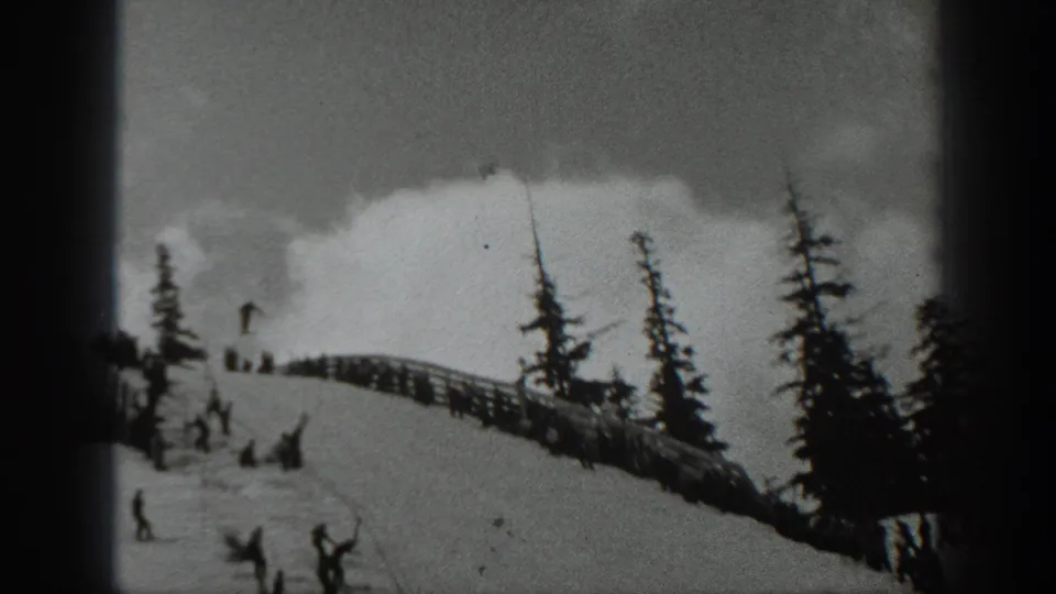 1940 Washington 8mm frame showing a snowy ski slope with evergreen trees, a fence line, and skiers or spectators gathered near the hill.