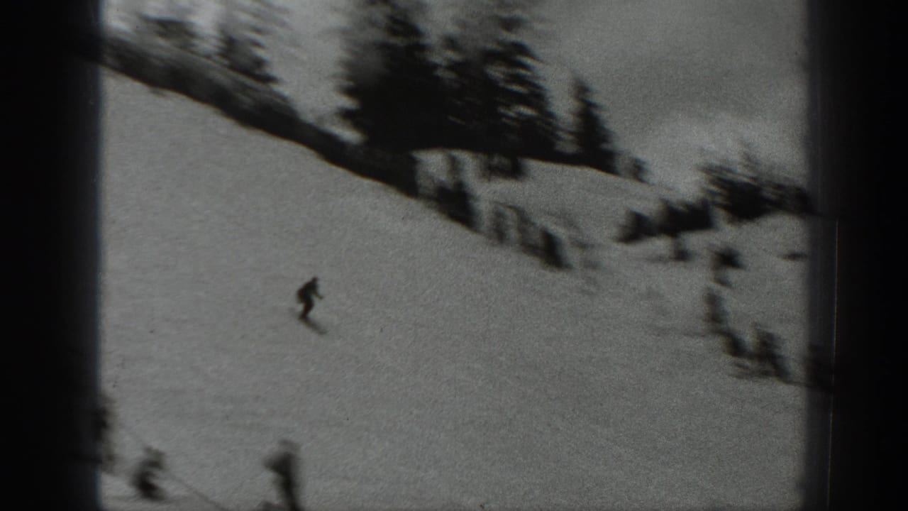 Skier moving down a snowy hill with blurred figures and trees near the slope edge.
