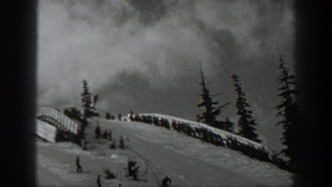 1940 Washington home-movie frame showing a snowy ski slope, evergreen trees, distant skiers, and a small crowd near slope infrastructure.