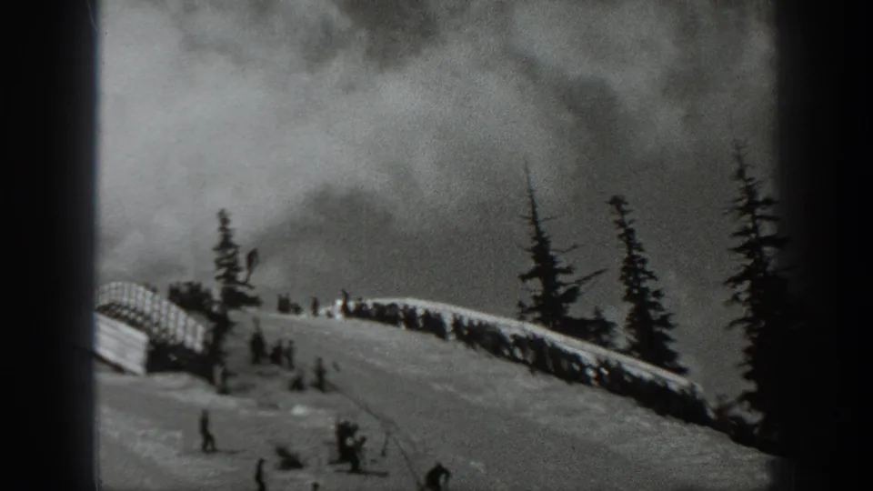 1940 Washington home-movie frame showing a snowy ski slope, evergreen trees, distant skiers, and a small crowd near slope infrastructure.