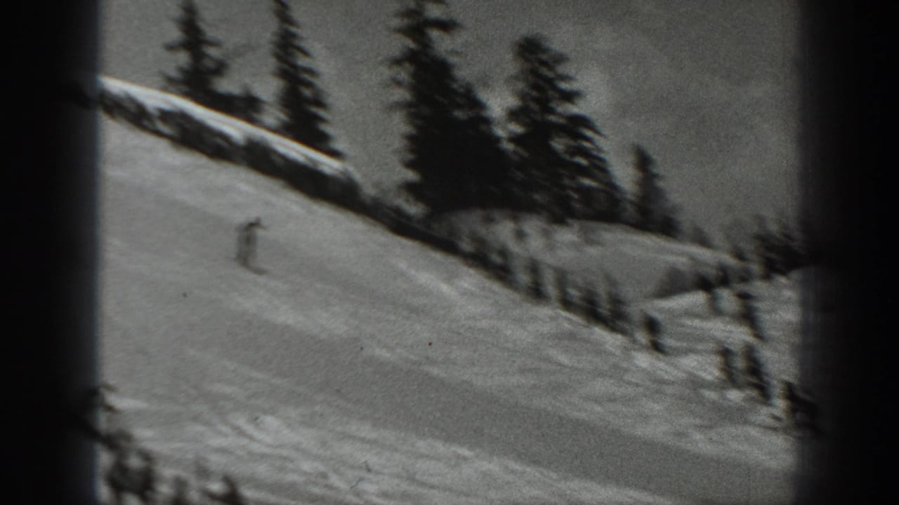 1940 Washington ski-resort footage frame with a skier on an open snowy slope and dark evergreen trees along the ridge.
