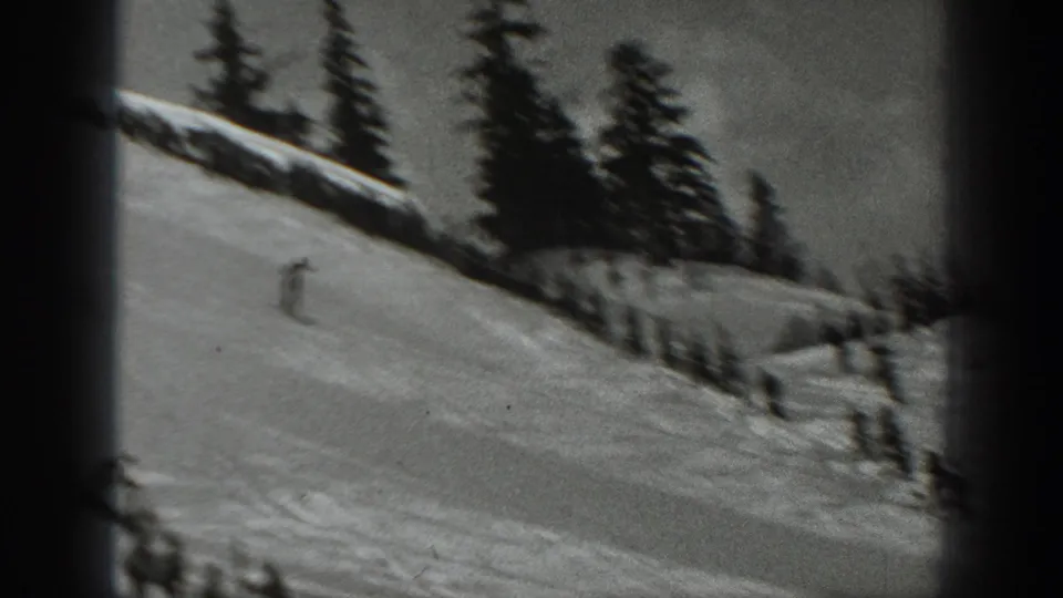 1940 Washington ski-resort footage frame with a skier on an open snowy slope and dark evergreen trees along the ridge.