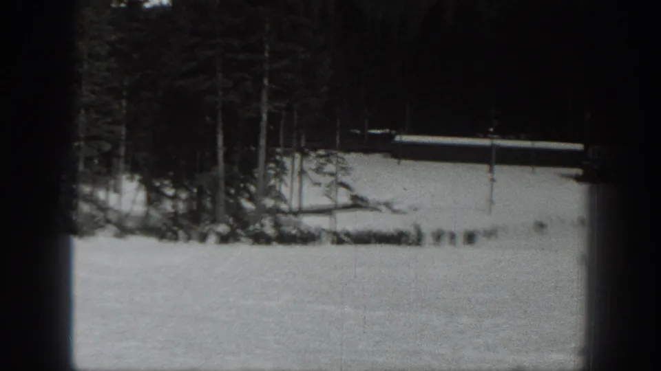 1940 Washington winter frame showing snow, forest edge, and a long low structure or fence, with tiny distant figures near the base.