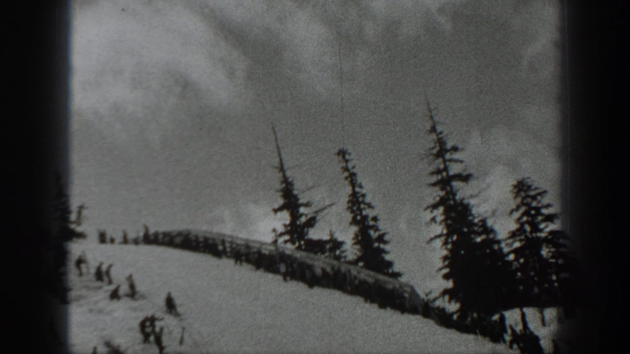 1940 Washington home-movie frame showing skiers descending a snowy hillside near evergreen trees and a low wooden structure.