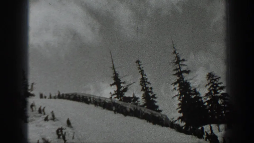 1940 Washington home-movie frame showing skiers descending a snowy hillside near evergreen trees and a low wooden structure.