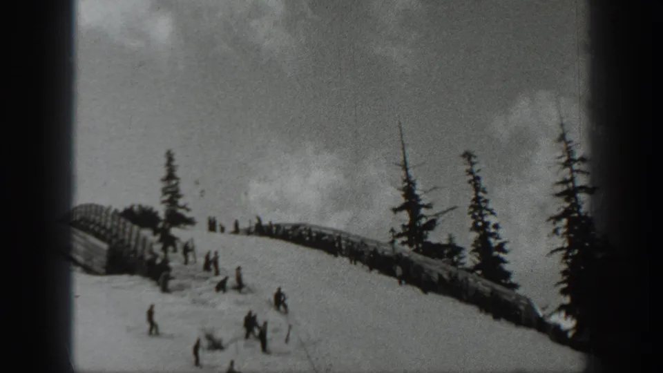 Archival black-and-white frame of skiers on a Washington snow slope in 1940, with trees and dark 8mm borders visible.