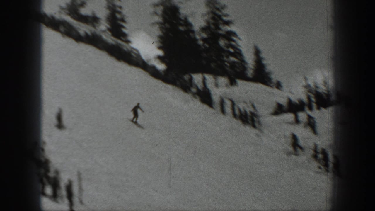 Black-and-white 1940 Washington 8mm frame showing a lone skier on a snowy hillside with evergreens and small figures below.