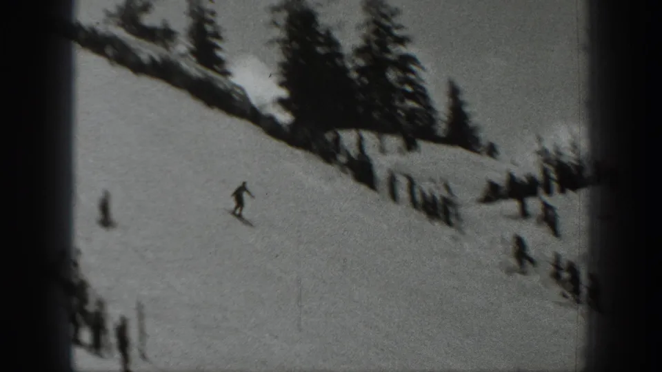 Black-and-white 1940 Washington 8mm frame showing a lone skier on a snowy hillside with evergreens and small figures below.