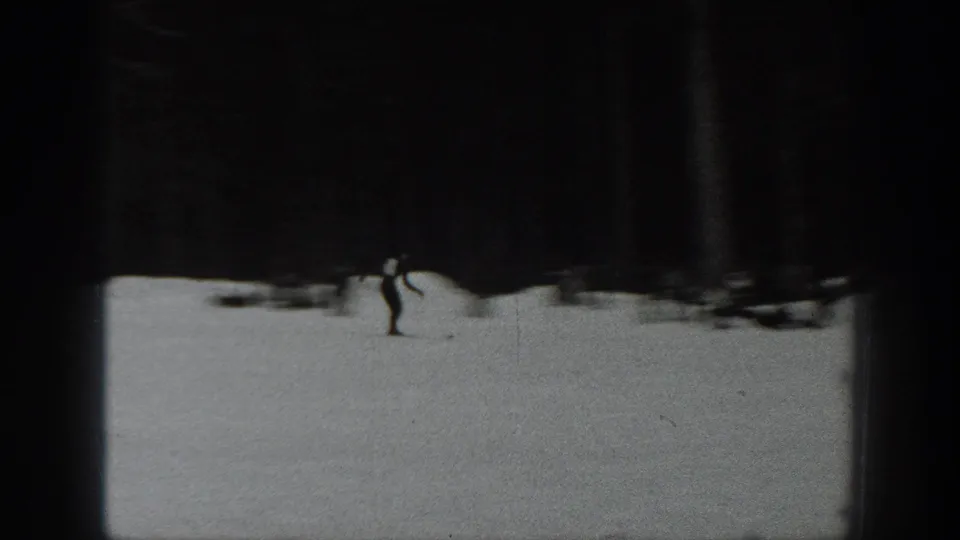 Black-and-white 1940 Washington 8mm frame with a distant skier moving across open snow below a dark evergreen forest.