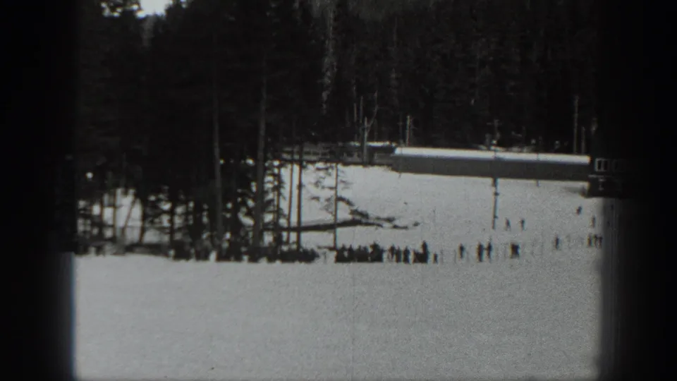 Black-and-white 1940 Washington 8mm frame showing a lower snowfield with distant people, trees, and a long structure near the slope.