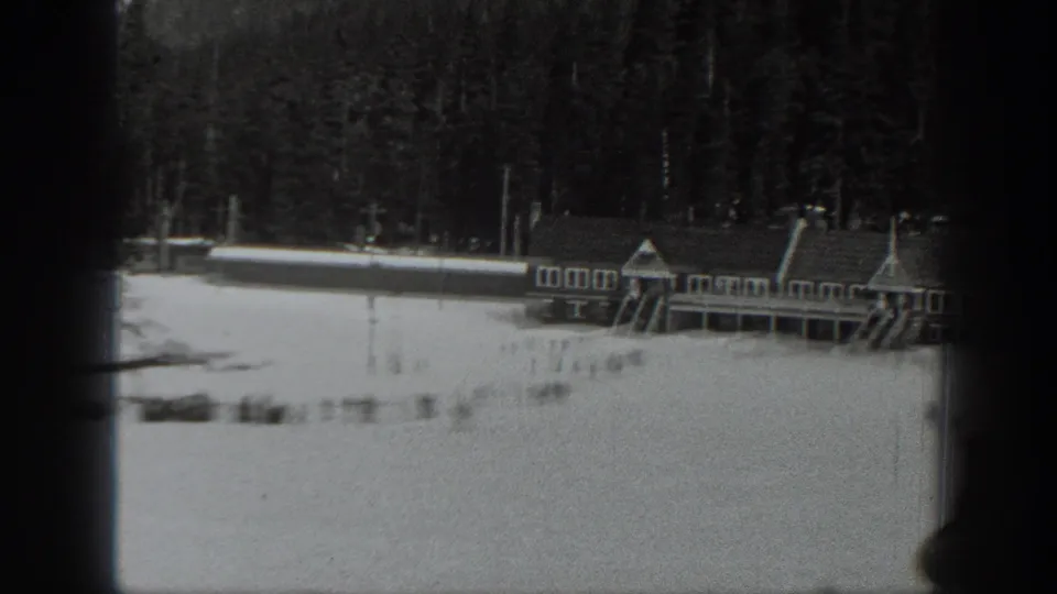 Black-and-white 1940 Washington home-movie frame showing a snow-covered resort building beside evergreen forest.